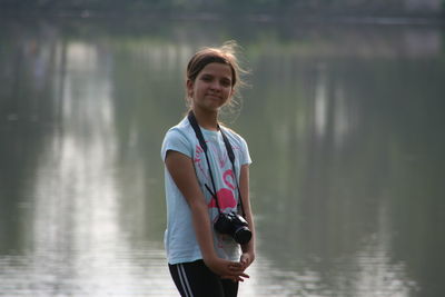 Portrait of girl with camera standing against lake