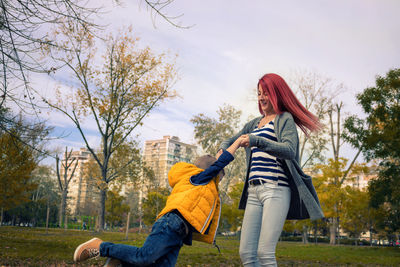 Low angle view of mother spinning son against sky in park