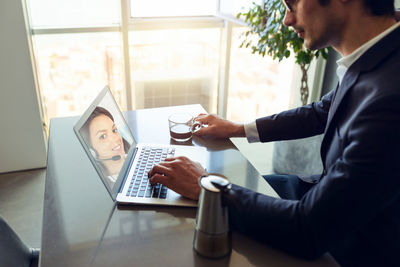 Man video conferencing with colleague over laptop on table