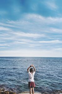 Rear view of girl standing at sea shore against blue sky