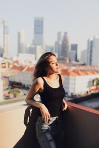 Young woman with eyes closed standing against building in terrace