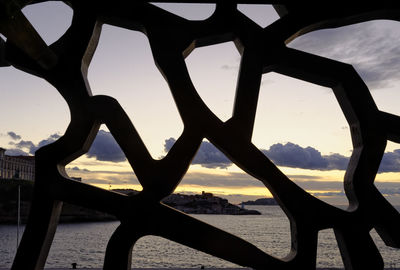 Silhouette metallic structure by sea against sky during sunset