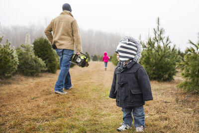 Toddler standing on grassy field with father carrying cordless chainsaw