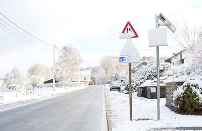 Road sign by snow in city against sky