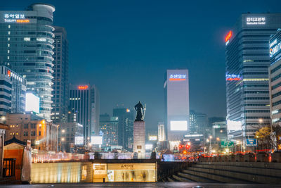 Statue on column amidst illuminated buildings against sky at night