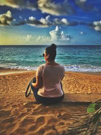 Rear view of boy sitting on beach against sky