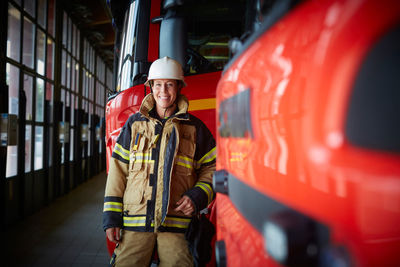 Portrait of smiling female firefighter standing by fire truck at fire station