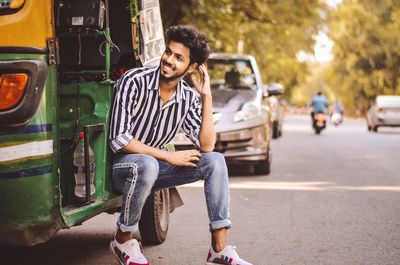 Full length portrait of young man sitting on road in city