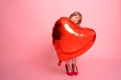 Beautiful child girl with big red heart balloon on pink background celebrating valentine day