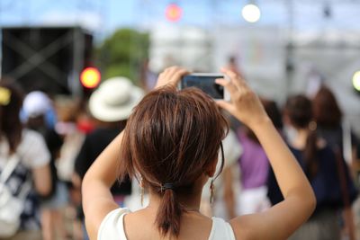 Rear view of woman photographing people through smart phone