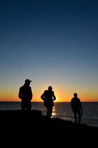 Silhouette people on beach against sky during sunset