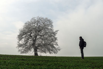Man standing by tree on field against sky