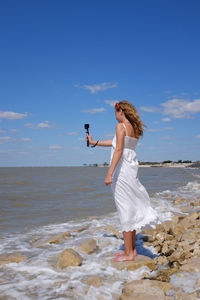 Full length of woman standing at beach against blue sky
