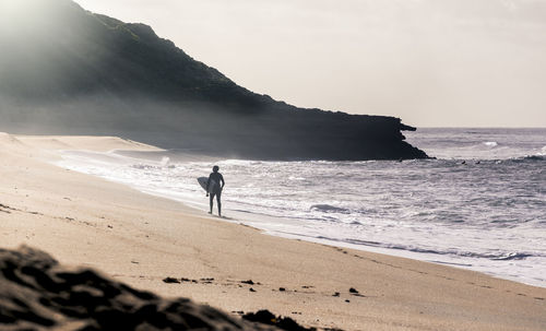 Silhouette man carrying surfboard at beach