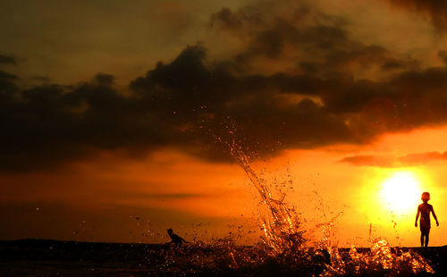 Silhouette man standing by sea against sky at sunset