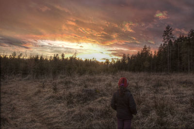 Rear view of woman standing on grassy field against sky during sunset