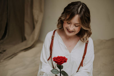 Young female in victorian shirt sitting with rose on the sand and smile