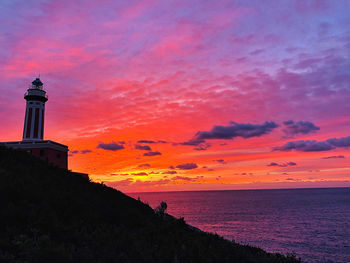 Silhouette lighthouse by sea against orange sky