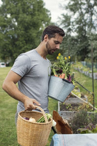 Mid adult man carrying buckets full of freshly harvested vegetables at urban garden