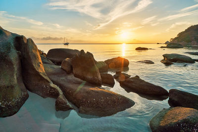 Rocks on beach against sky during sunset