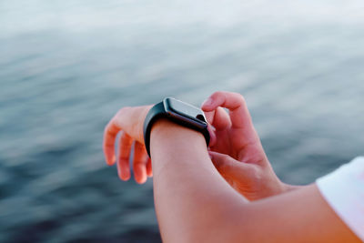 Cropped hand of person wearing smart watch against sea