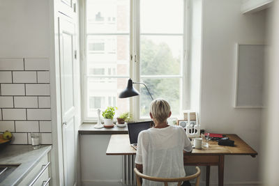 Rear view of industrial designer using laptop at table by window