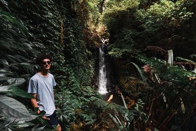 Young man standing by waterfall in forest