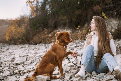 Young woman and dog retriever walks on river shore at autumn season