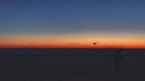 Silhouette man on beach against clear sky during sunset