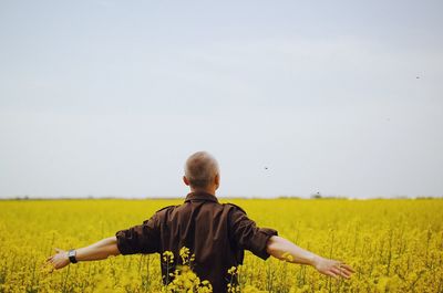 Rear view of man standing on rapeseed field against sky