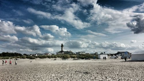 People on beach against cloudy sky
