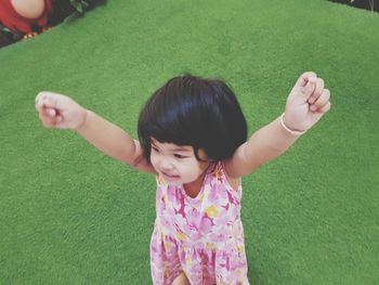 High angle view of cute girl with arms raised standing on turf