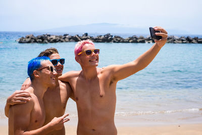 Shirtless boys doing selfie while standing at beach