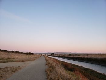 Empty road amidst field against clear sky