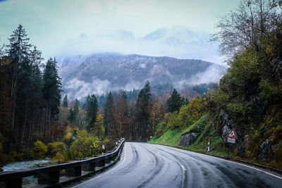 Country road by trees against sky