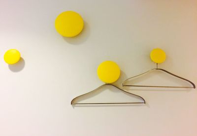 Coathangers hanging from yellow knobs mounted on white wall