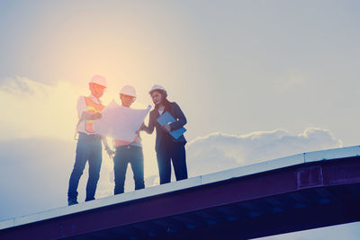 Low angle view of people standing on bridge against sky