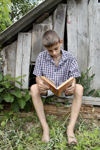 A boy sits near a wooden old booth and reads a book