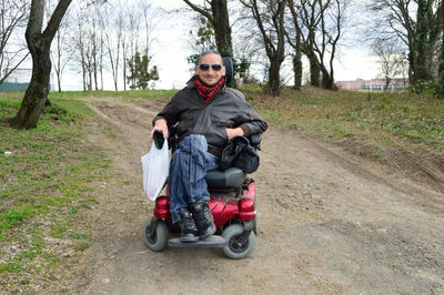 Portrait of smiling man sitting on wheelchair at dirt road