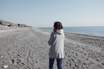 Back view of woman walking on the deserted winter beach, enjoying sunny weather