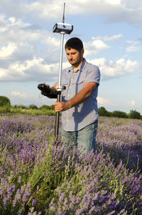 Surveyor with theodolite on lavender field against sky