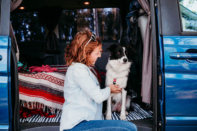 Woman with dog sitting at entrance of camper trailer