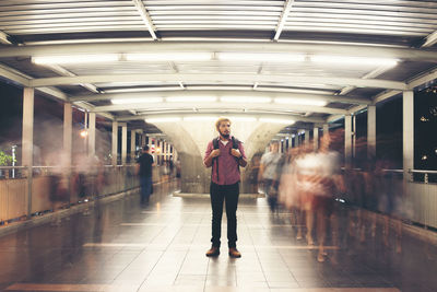 Young man looking away while standing on illuminated footbridge at night