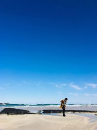 Man standing on beach against blue sky