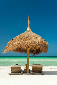 Deck chairs and thatched umbrella at beach against clear blue sky