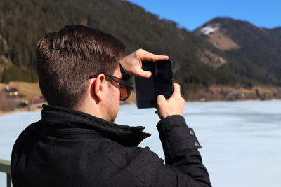 Young man photographing frozen lake from mobile phone