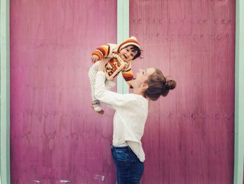 Mother lifting daughter while standing against wall