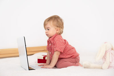 Blonde aby girl,toddler on bed looking at laptop in white scandinavian space