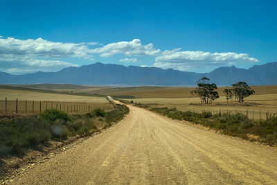 Dirt road leading towards mountains against sky