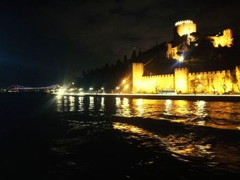 Illuminated buildings by river against sky at night